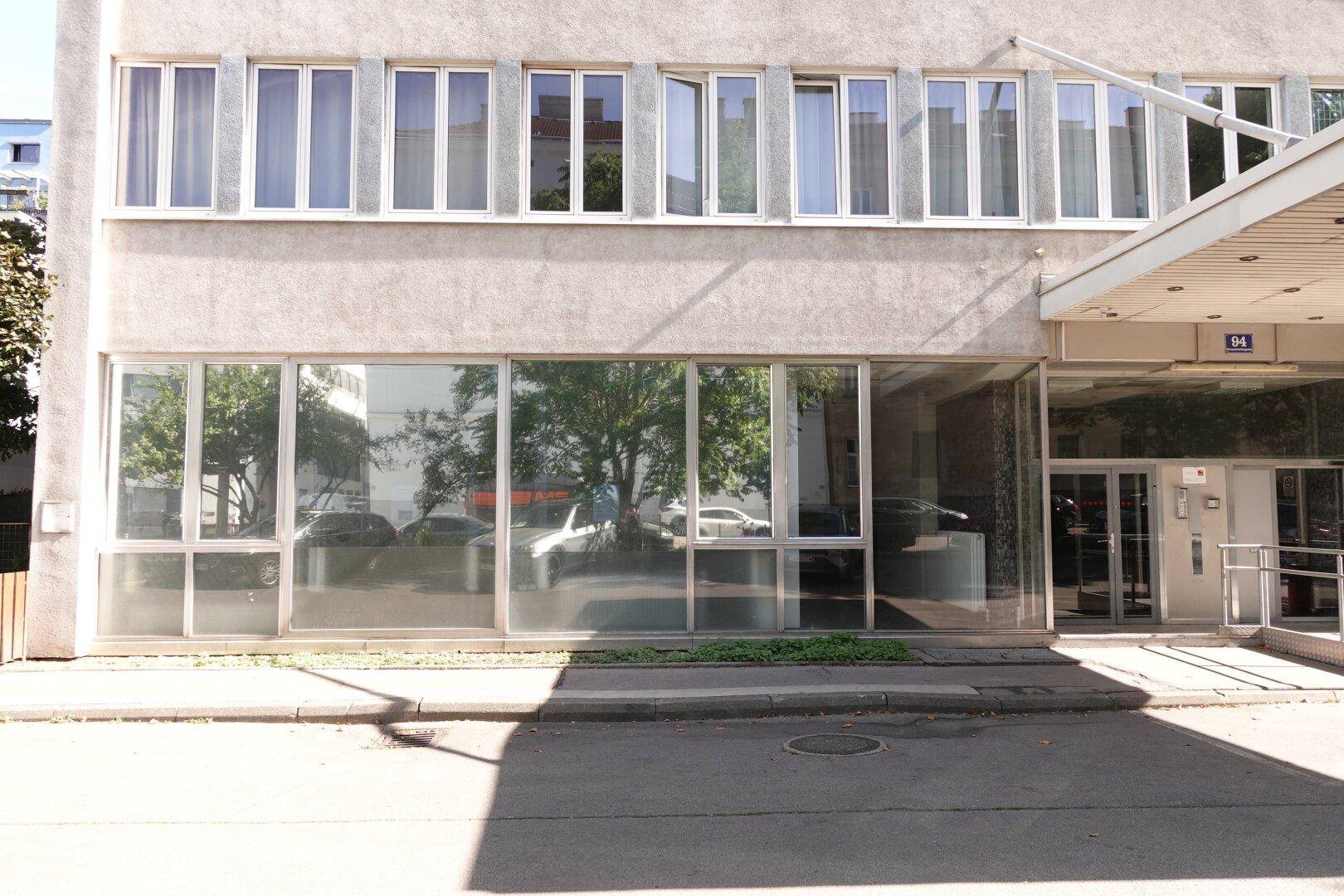 Erdgeschossfassade eines modernen Gebäudes mit großen Schaufenstern und einem klaren Eingangsbereich.