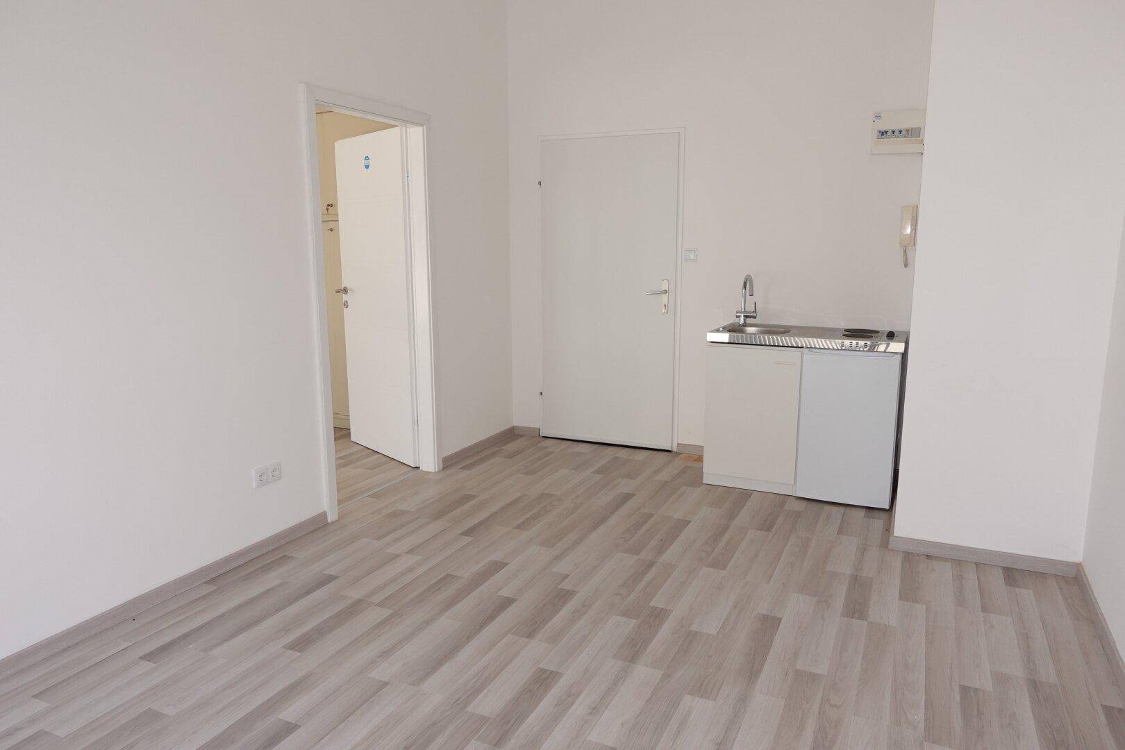 Heller Raum mit kleiner Küchenzeile, Spüle und Laminatboden, ideal für eine Büronutzung.