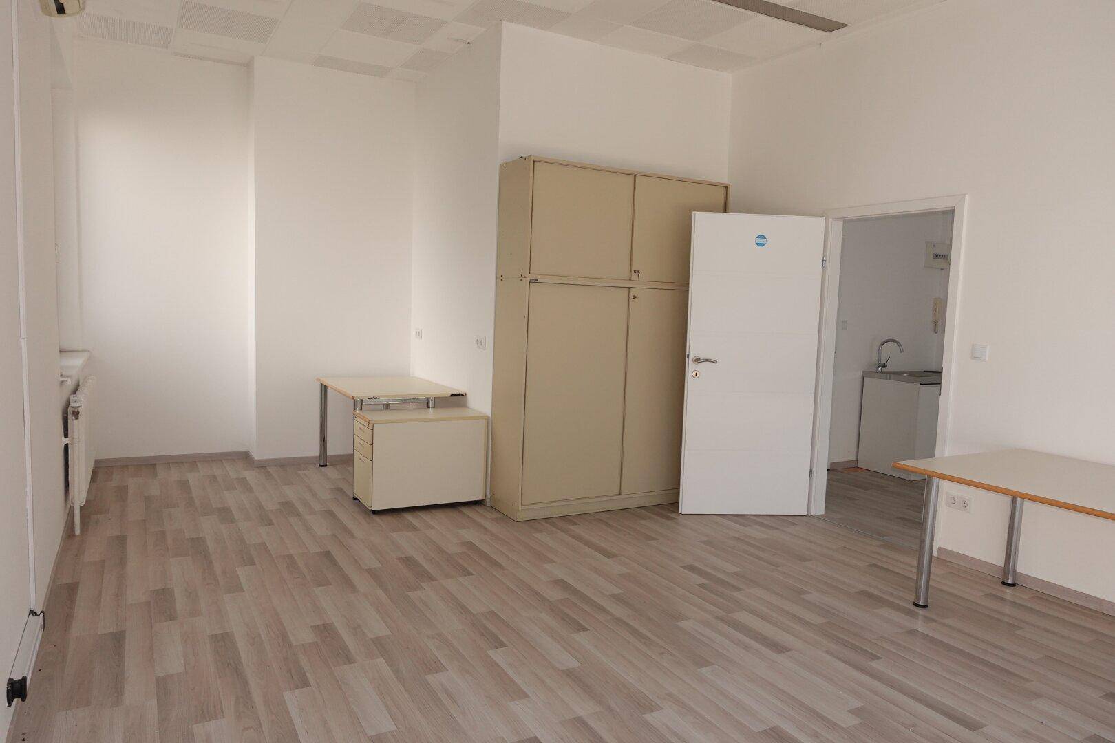Geräumiger Büroraum mit Laminatboden, Schränken und Zugang zu einem Nebenraum mit Spüle.