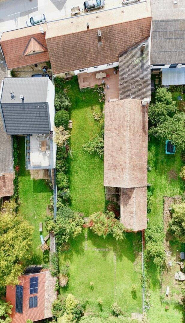 Luftaufnahme eines Anwesens mit langgestrecktem Gebäude, großem Garten und umliegenden Häusern.