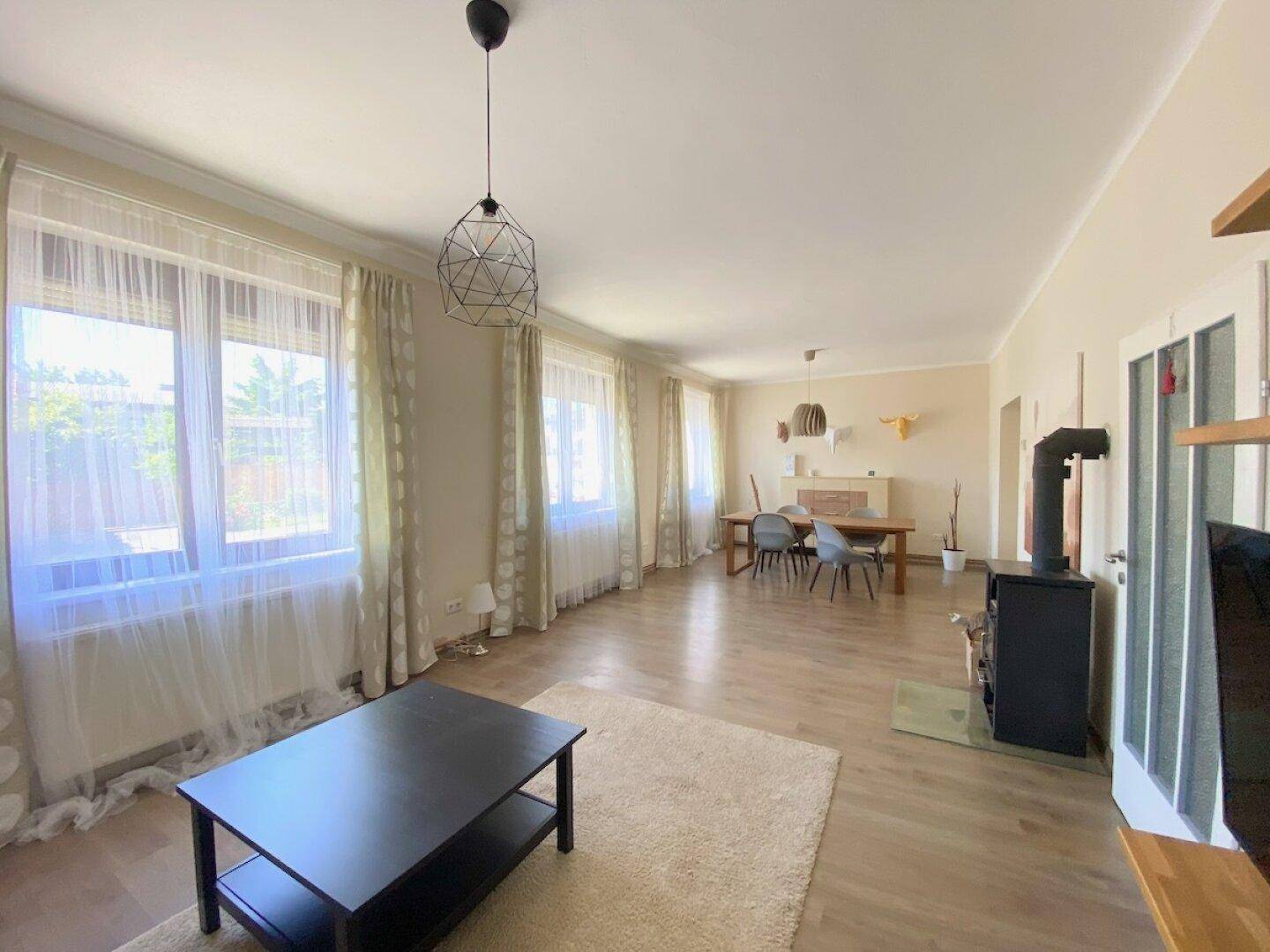 Heller Wohn-Essbereich mit großen Fenstern, Laminatboden und einem Kaminofen.