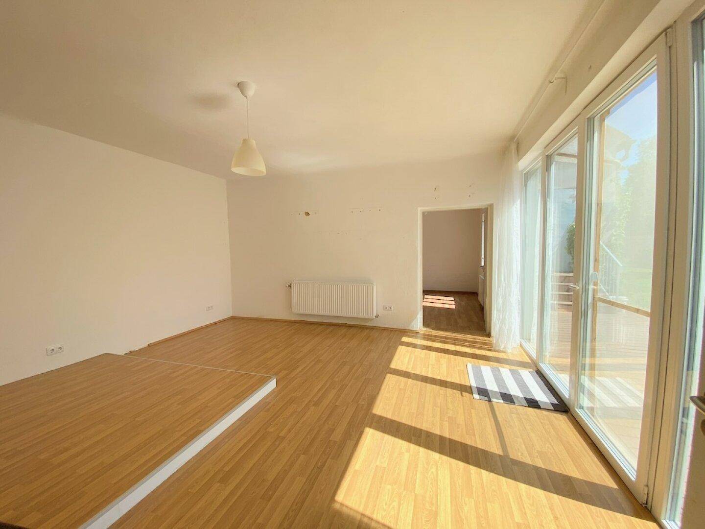 Lichtdurchfluteter Wohnraum mit großen Fenstern und hellem Holzboden.