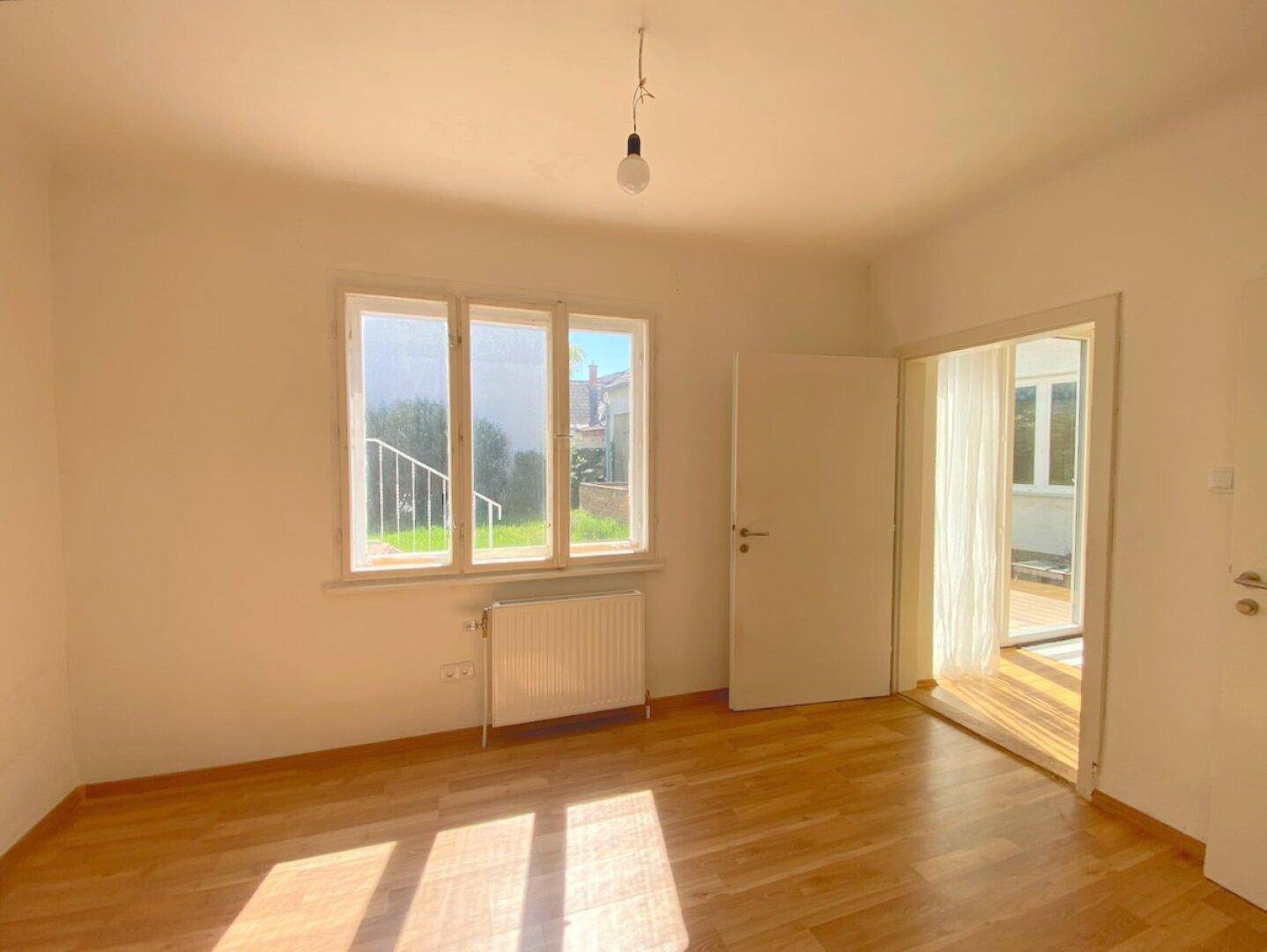 Heller Raum mit Holzboden und Blick auf den grünen Garten durch das Fenster.