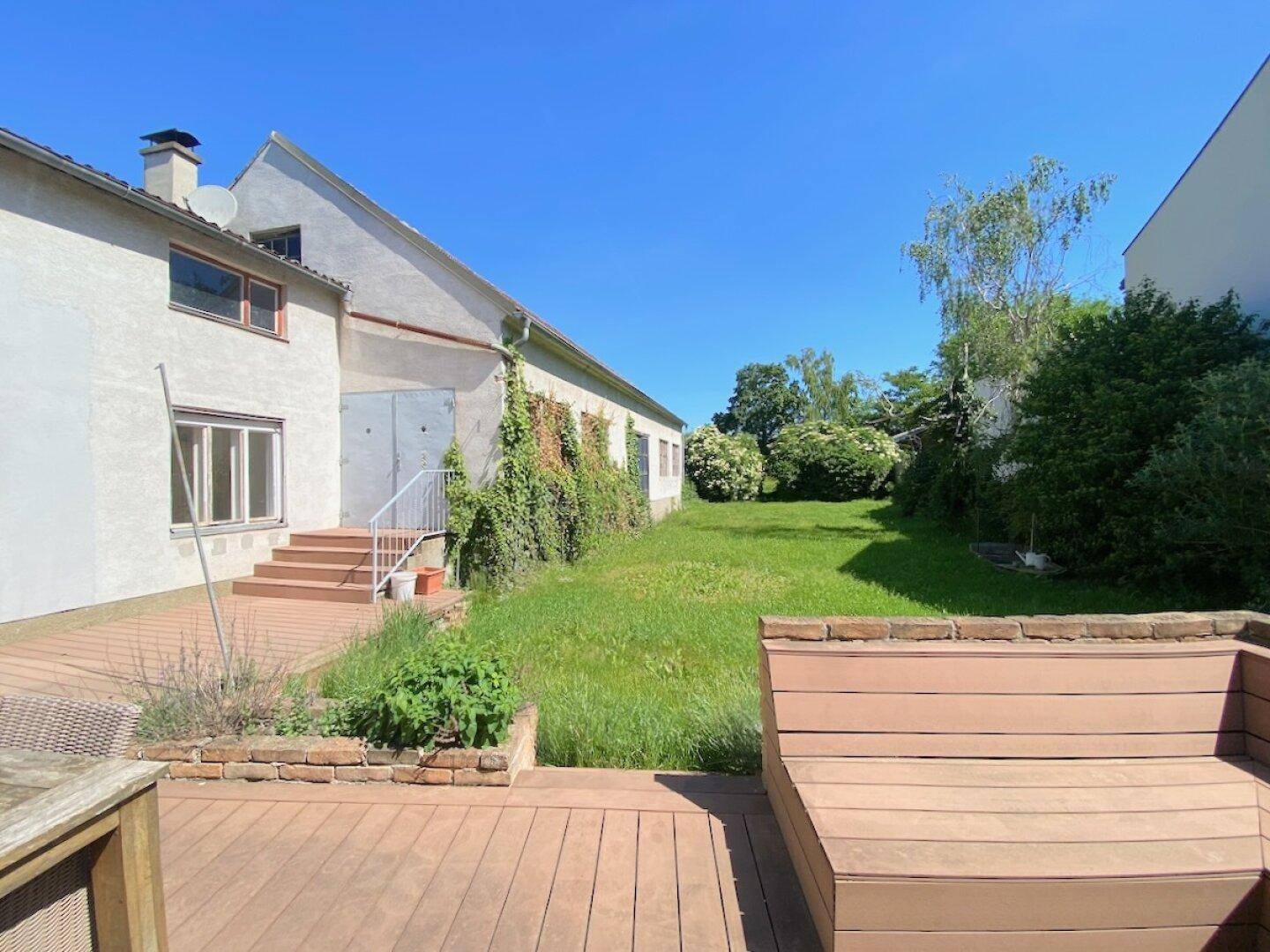 Geräumige Holzterrasse mit Blick auf den grünen Garten und das Gebäude.