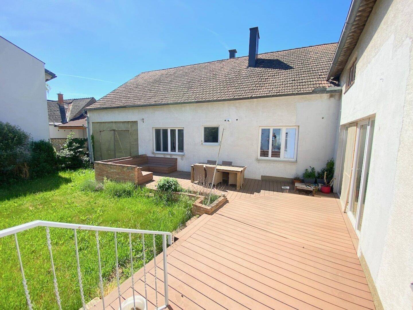 Holzterrasse mit Gartenblick und Zugang zu einem Nebengebäude.