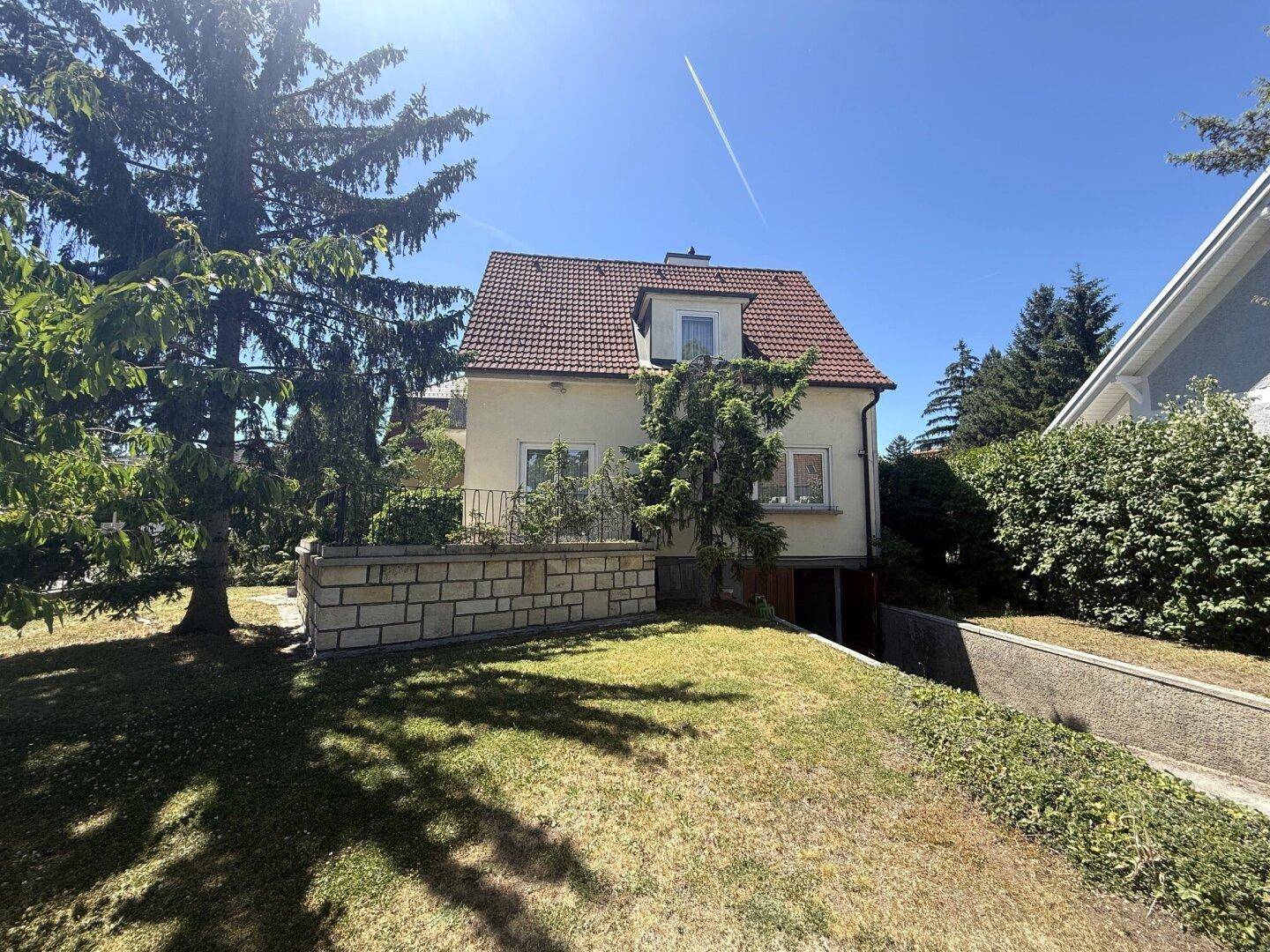 Gesamtansicht des Hauses mit großem Garten, Zufahrt und umgebenden Bäumen unter blauem Himmel.