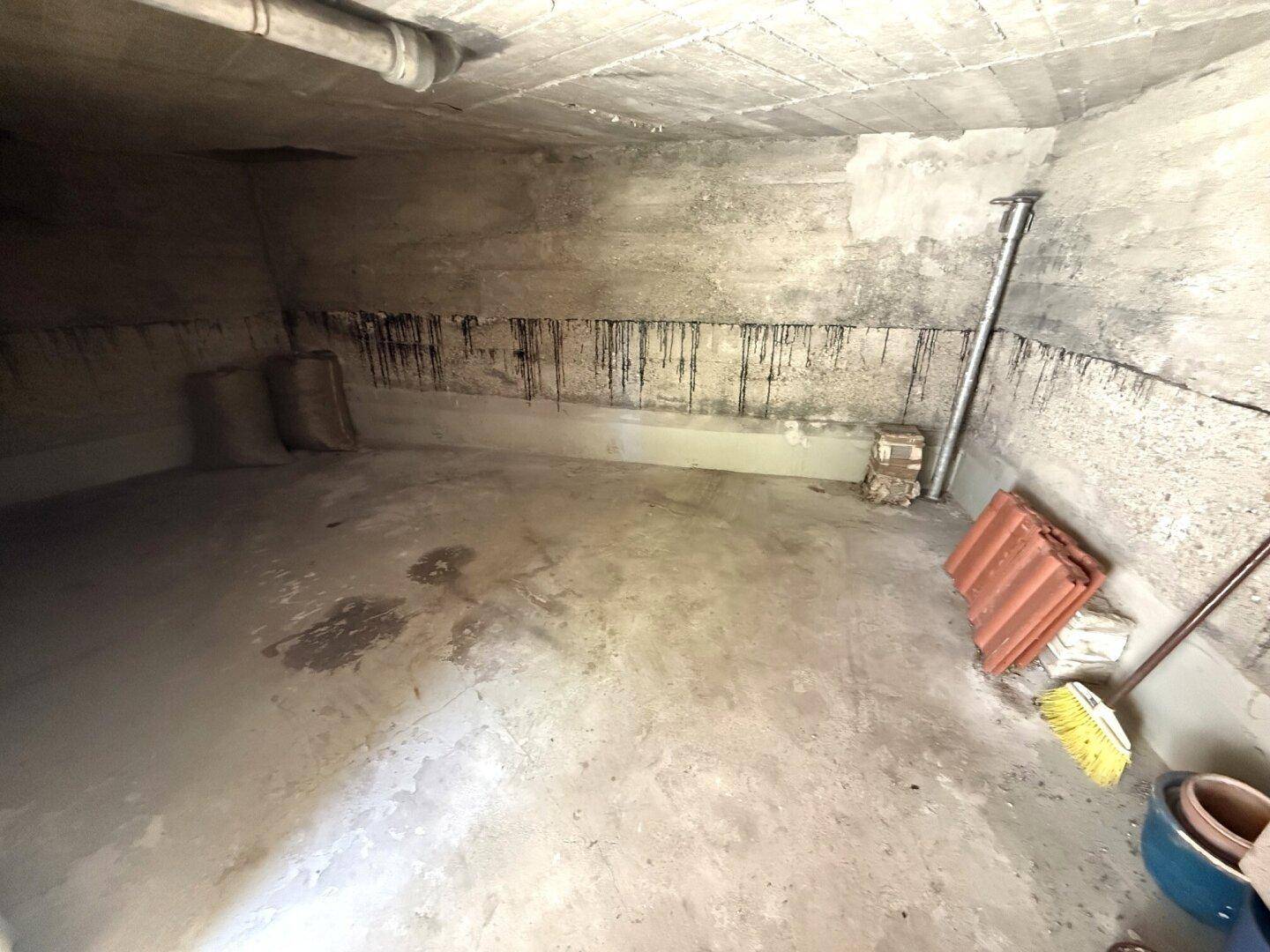 Kellerraum mit Betonboden und Spuren von Feuchtigkeit an den Wänden.