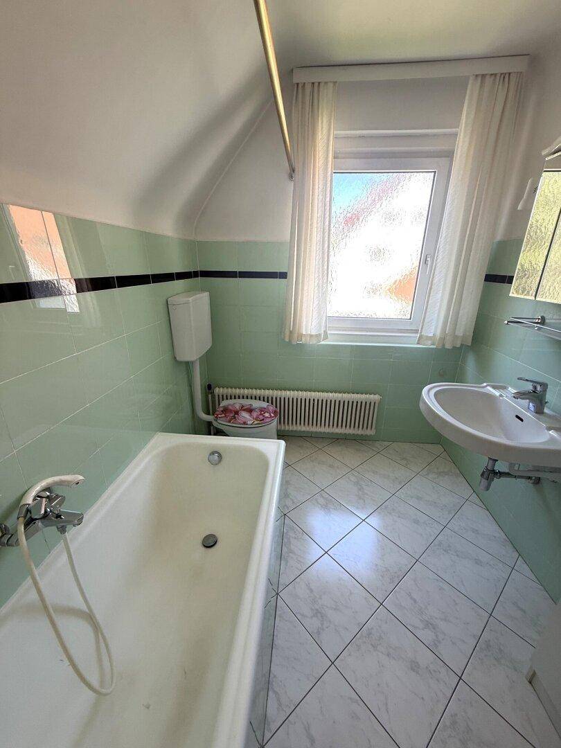 Badezimmer mit mintgrünen Fliesen, Badewanne, Waschbecken und Fenster.