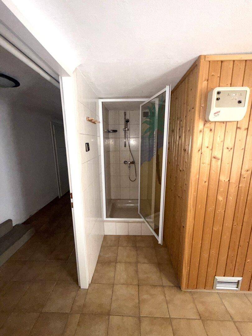 Duschbereich mit Fliesen und Holzverkleidung, angrenzend an die Sauna.
