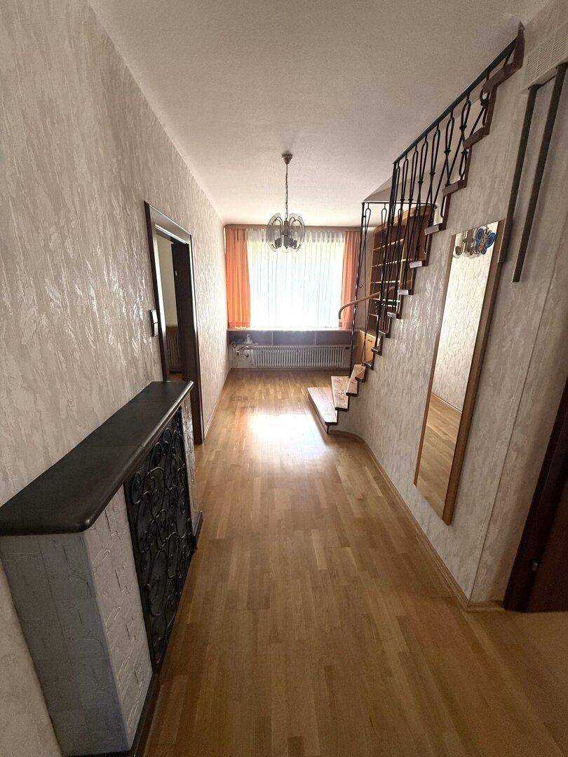 Flur mit Parkettboden, Treppe und großem Wandspiegel.