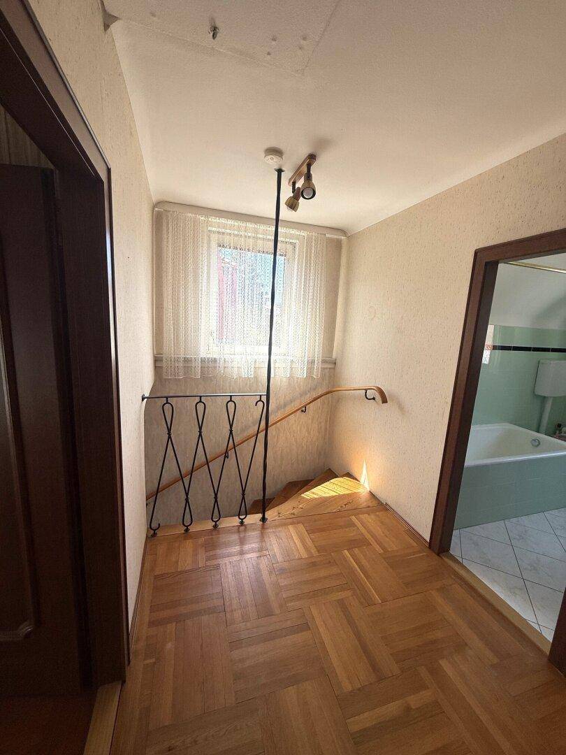 Oberer Flur mit Parkettboden, Fenster und Blick ins Badezimmer.
