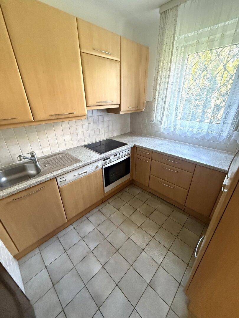 Funktionale Küche mit hellen Holzschränken, Fliesenboden und Fenster.