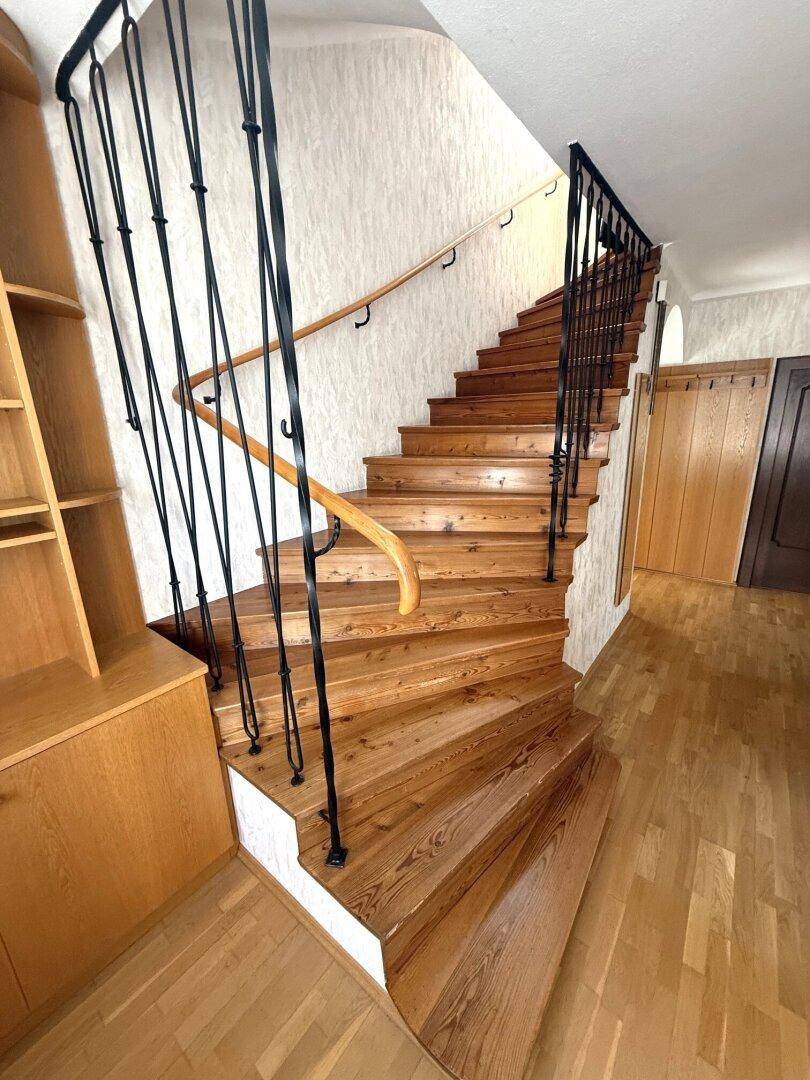 Geschwungene Holztreppe mit schmiedeeisernem Geländer und Holzregal.