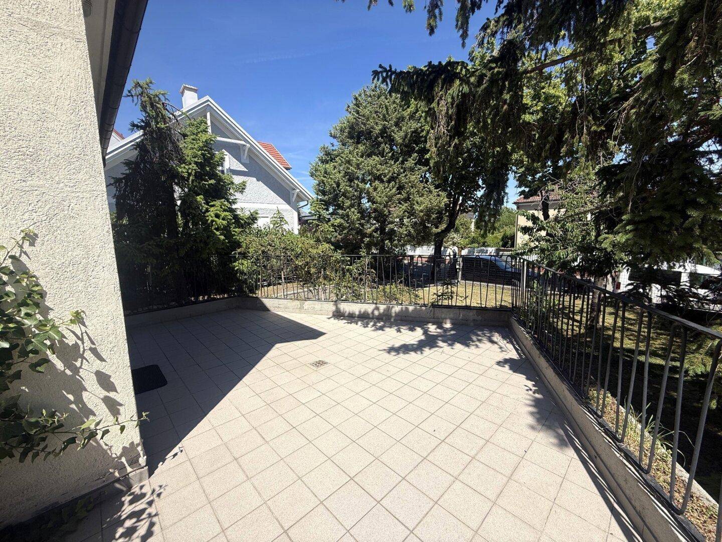 Geflieste Terrasse mit Metallgeländer und umgebender Bepflanzung.