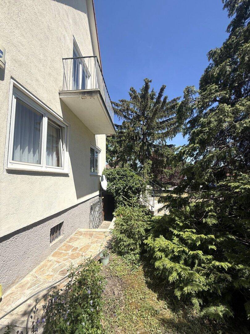 Seitlicher Zugang zum Haus mit Steintreppe, Balkon und üppiger Bepflanzung.