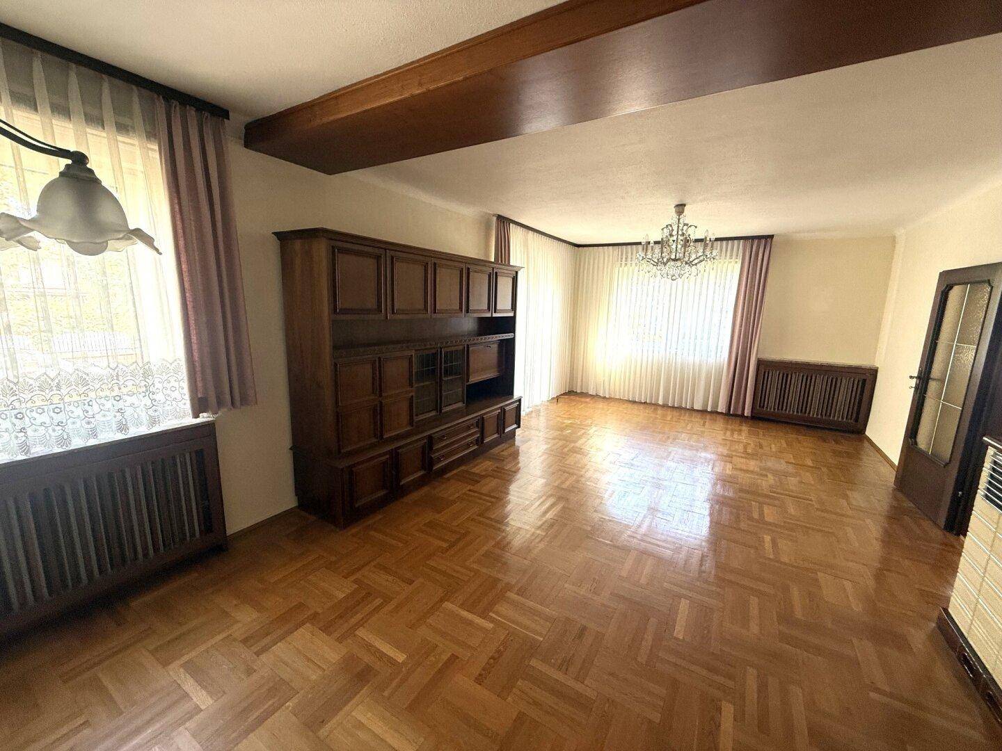 Geräumiges Wohnzimmer mit Fischgrätparkett, Holzeinbauschrank und Kronleuchter.