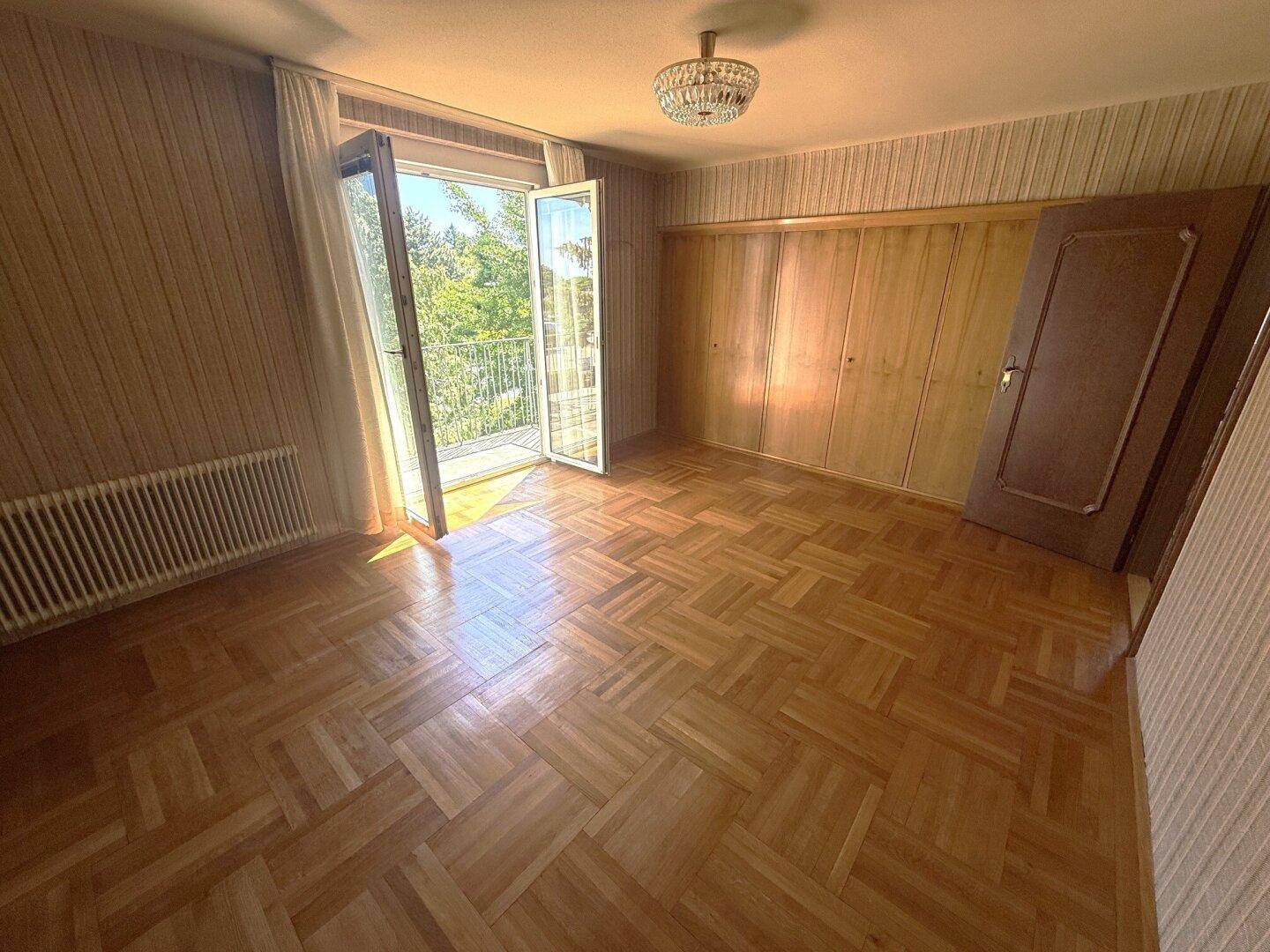 Schlafzimmer mit Parkettboden, Zugang zum Balkon und integrierten Holzschränken.