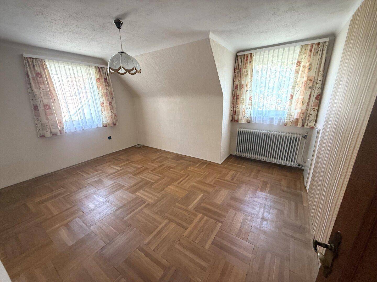 Helles Schlafzimmer mit Parkettboden, zwei Fenstern und Dachschräge.