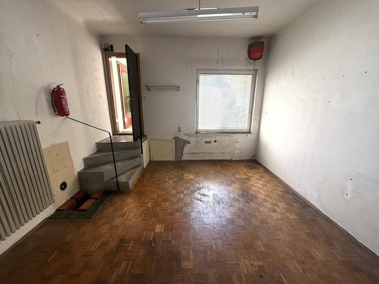 Unfertiger Raum mit Parkettboden, Treppe und Fenster, renovierungsbedürftig.