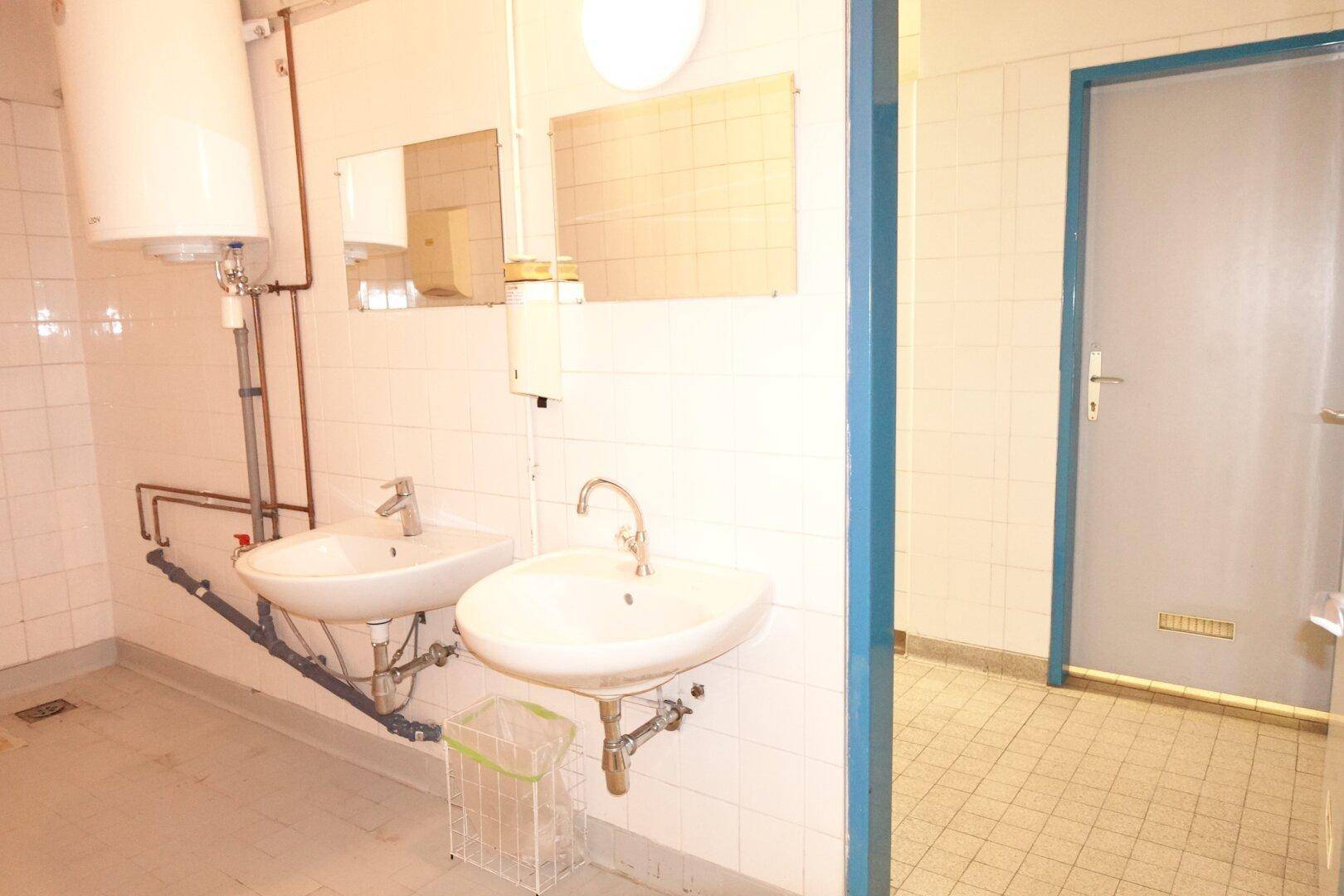 Funktionaler Waschraum mit zwei Waschbecken, einem Warmwasserboiler und gefliesten Wänden.
