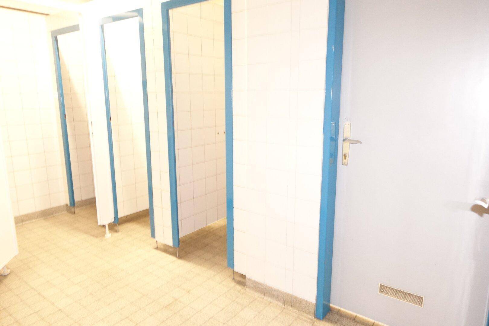 Mehrere Toilettenkabinen in einem öffentlichen Waschraum mit gefliesten Wänden und Böden.