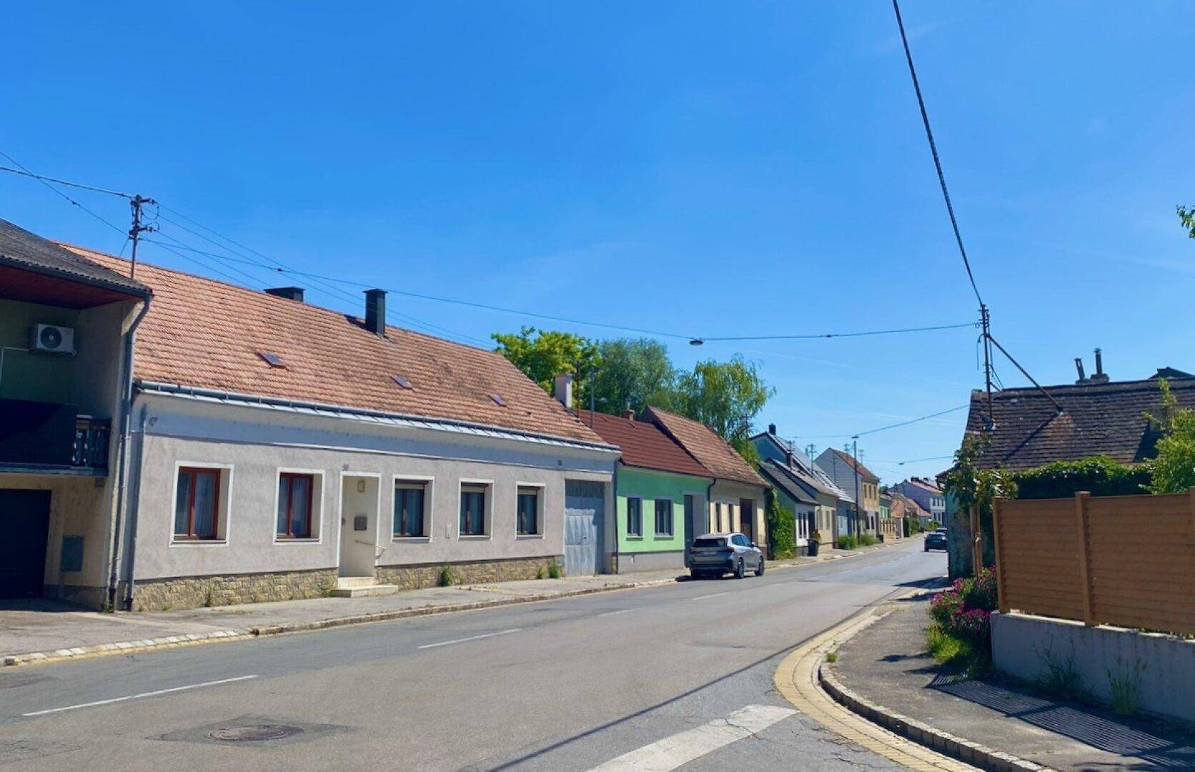 Wohnstraße in einem Dorf mit einer Mischung aus traditionellen und neueren Häusern unter blauem Himmel.