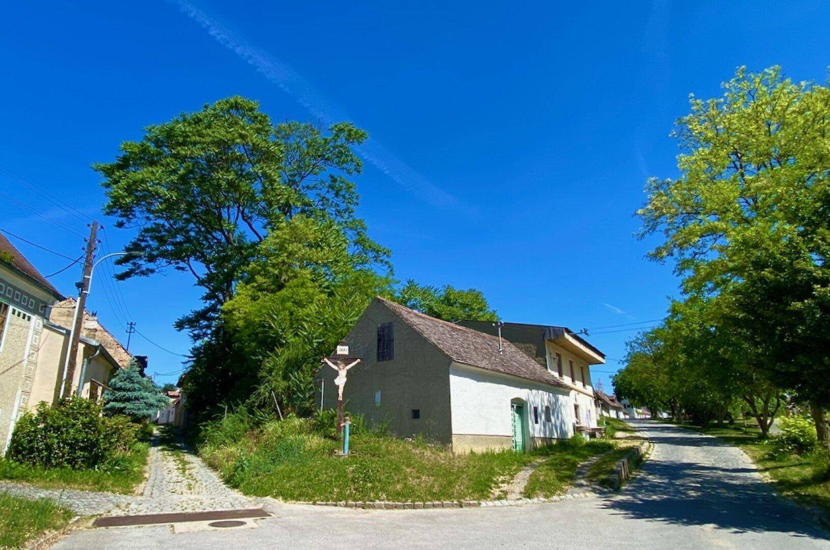 Ländliche Kreuzung in einem historischen Dorf mit traditionellen Häusern und einem markanten Kruzifix.