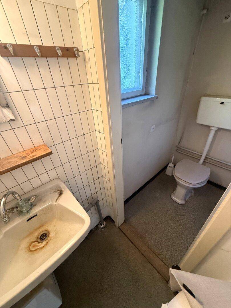 Einfache Toilette mit Waschbecken und Fenster, zeigt Gebrauchsspuren.