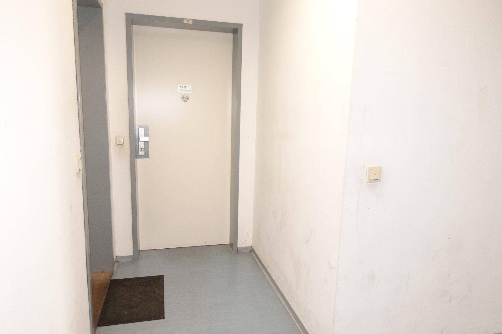 Eingangsbereich mit blauer Bodenfläche und weißer Tür, die in die Wohnung führt.