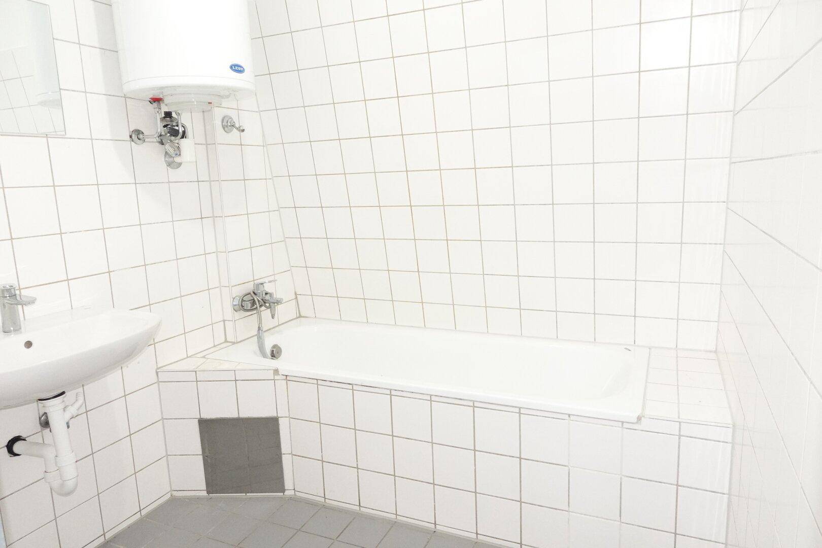 Einfaches Badezimmer mit Badewanne, Waschbecken und weißen Fliesen, funktional und sauber.