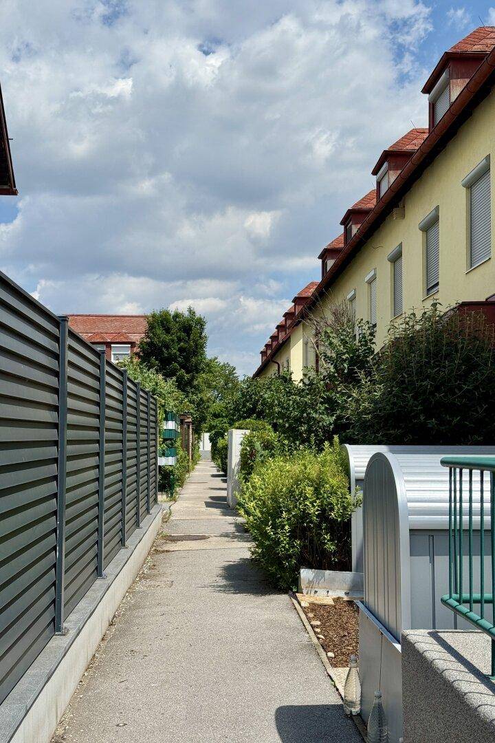 Schmaler Fußweg zwischen Reihenhäusern mit seitlichem Blick auf die Gebäude.