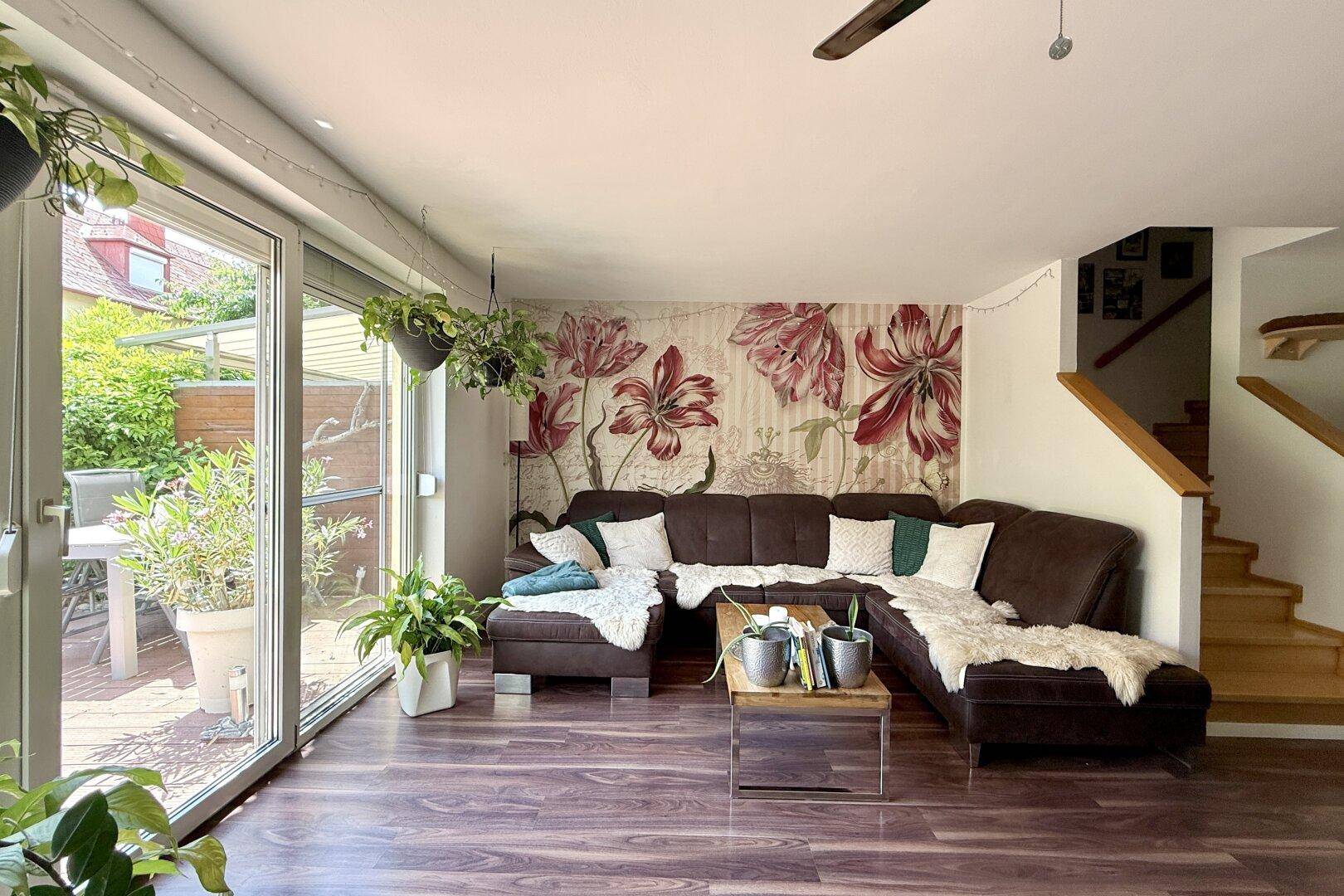 Helles Wohnzimmer mit großem Ecksofa, floraler Tapete und Zugang zur Terrasse.