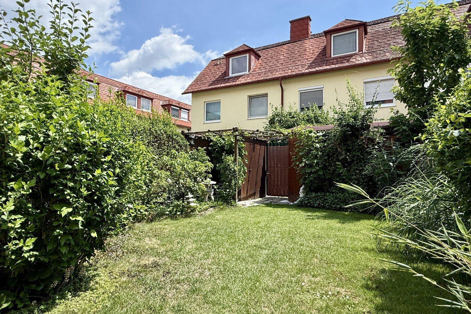 Gepflegter Garten mit Rasenfläche und üppiger Bepflanzung hinter dem Wohnhaus.