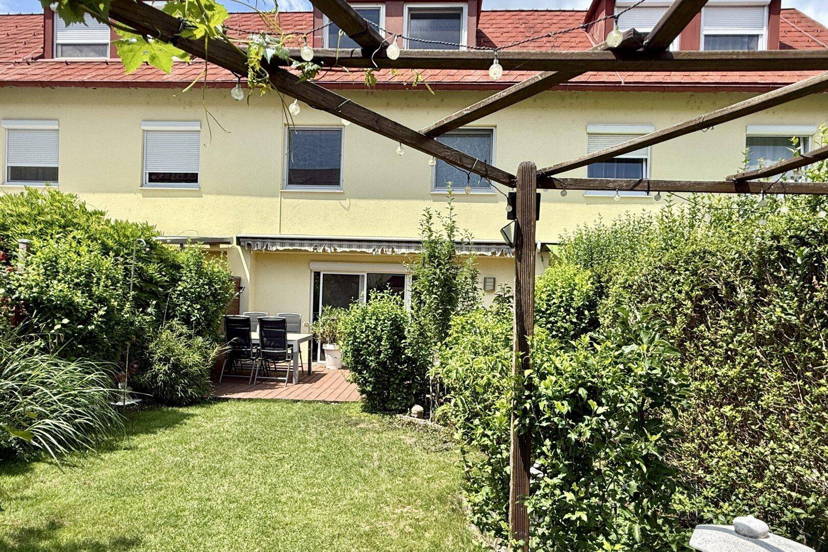 Gemütliche Terrasse mit Gartenmöbeln und Rasenfläche hinter dem Reihenhaus.