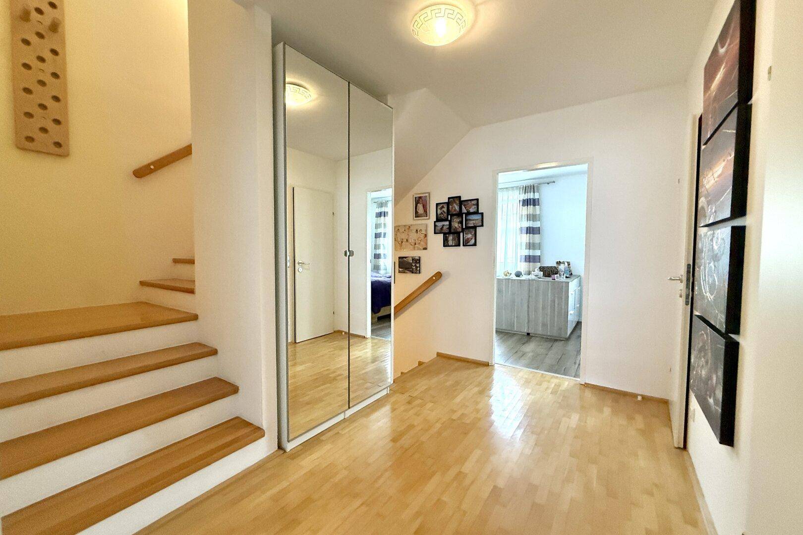 Heller Flur mit Holztreppe, Spiegelschrank und Zugang zu weiteren Räumen.