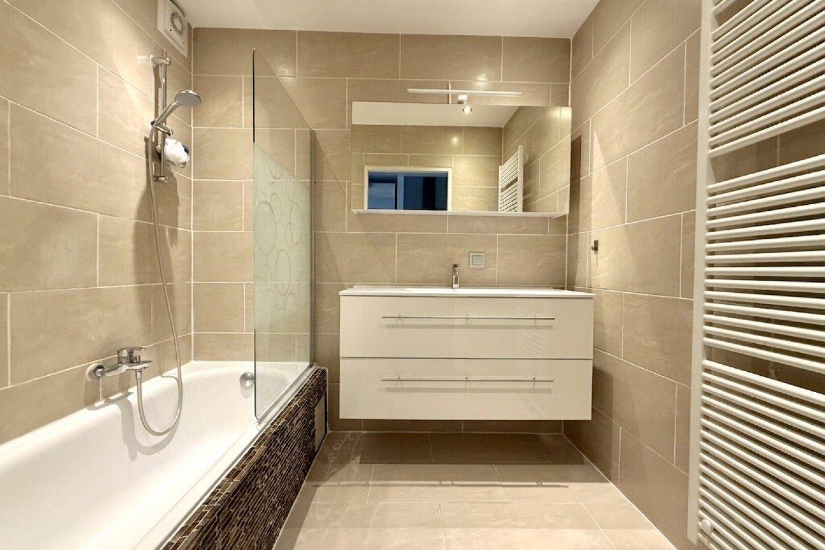 Modernes Badezimmer mit beigefarbenen Fliesen, Badewanne und Waschtisch.