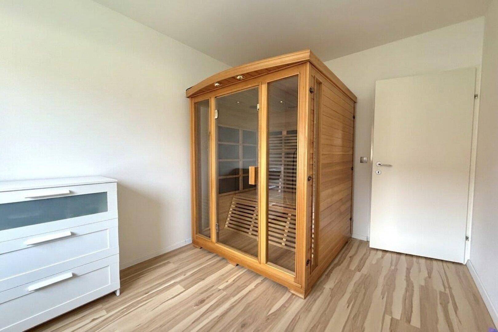 Raum mit einer modernen, freistehenden Sauna aus hellem Holz und Glas.