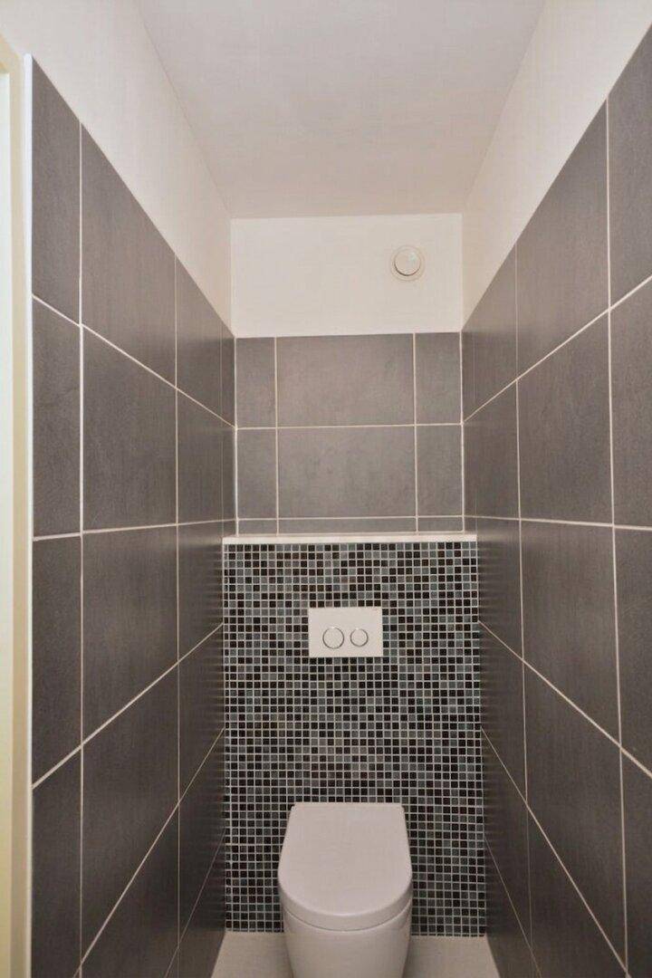 Kleines Gäste-WC mit dunklen Fliesen und wandhängendem WC.