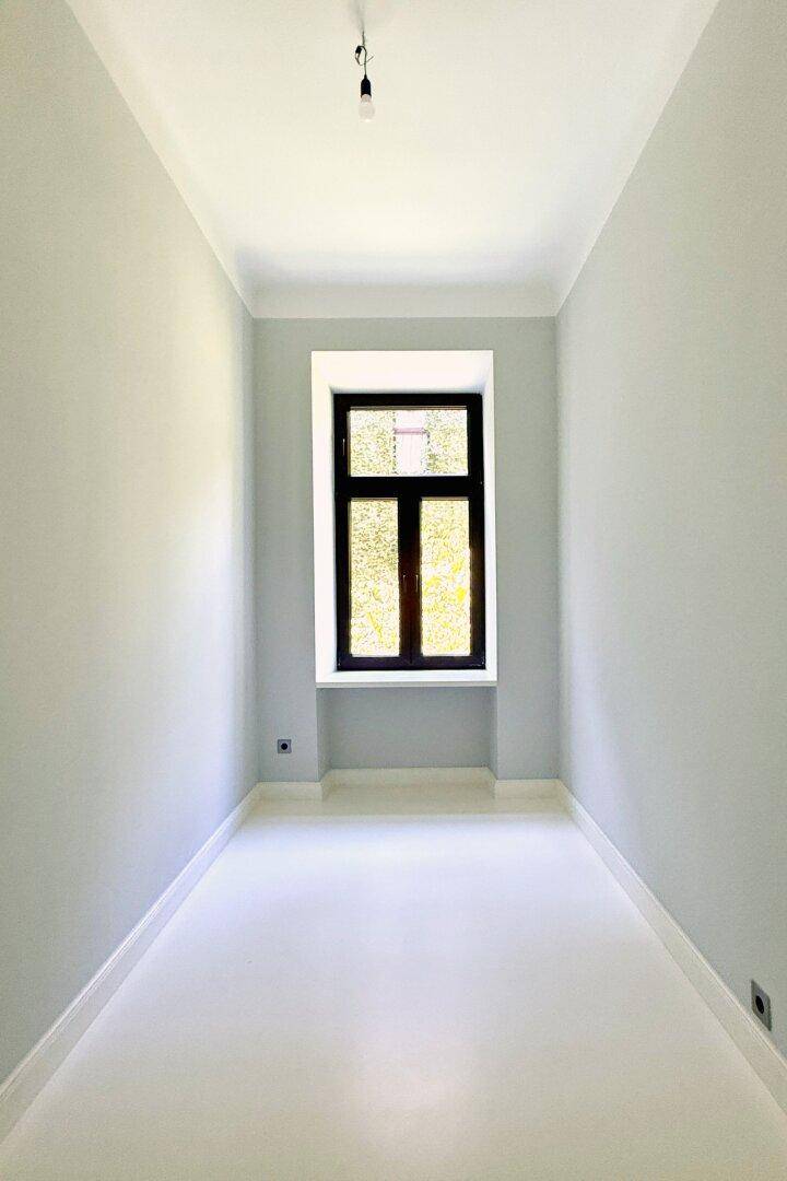 Leerer, heller Raum mit einem großen Fenster und hohen Decken, bereit zur individuellen Gestaltung.