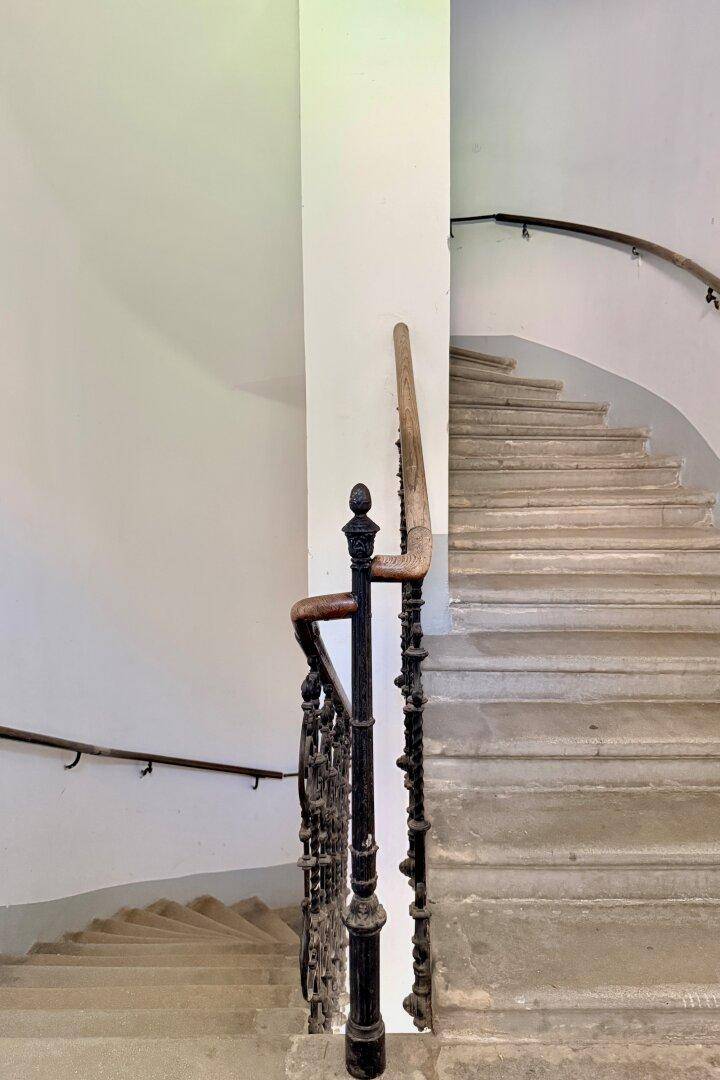 Historisches Treppenhaus mit kunstvollem Geländer und Steinstufen in einem Altbau.