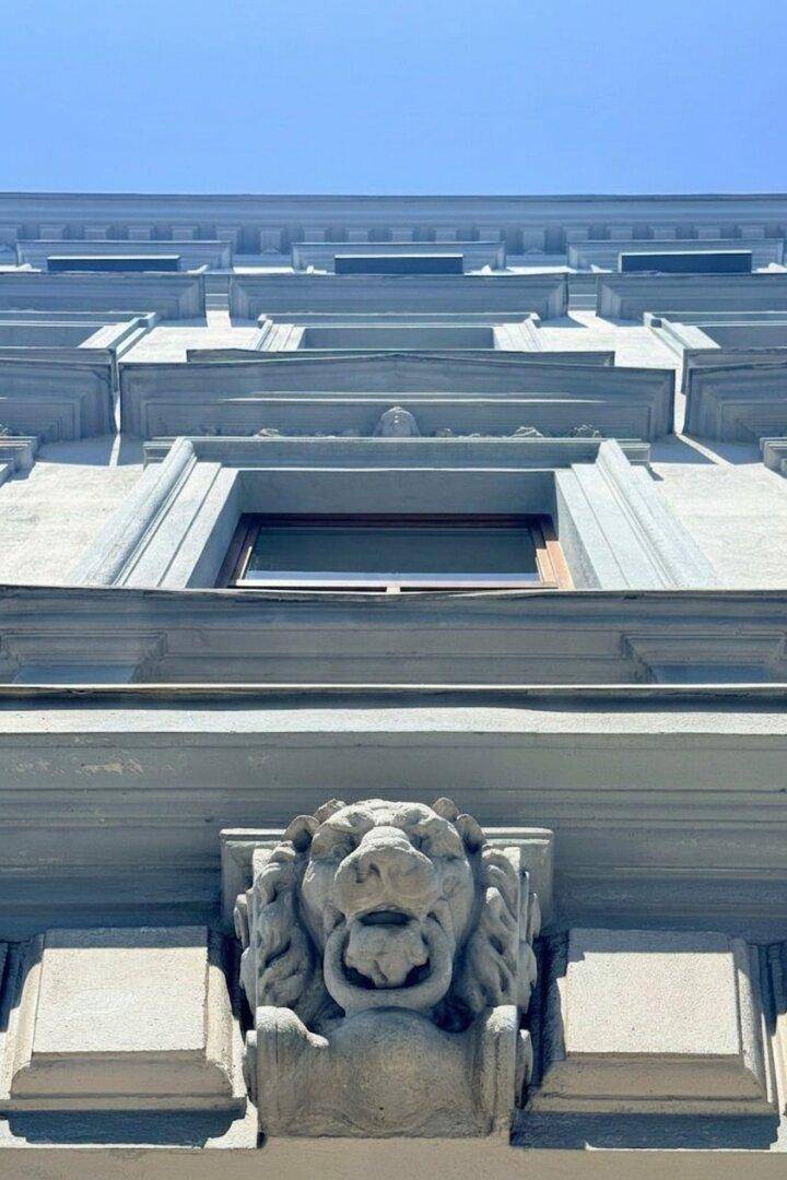 Detailaufnahme einer historischen Fassade mit kunstvoller Löwenkopf-Skulptur unter blauem Himmel.