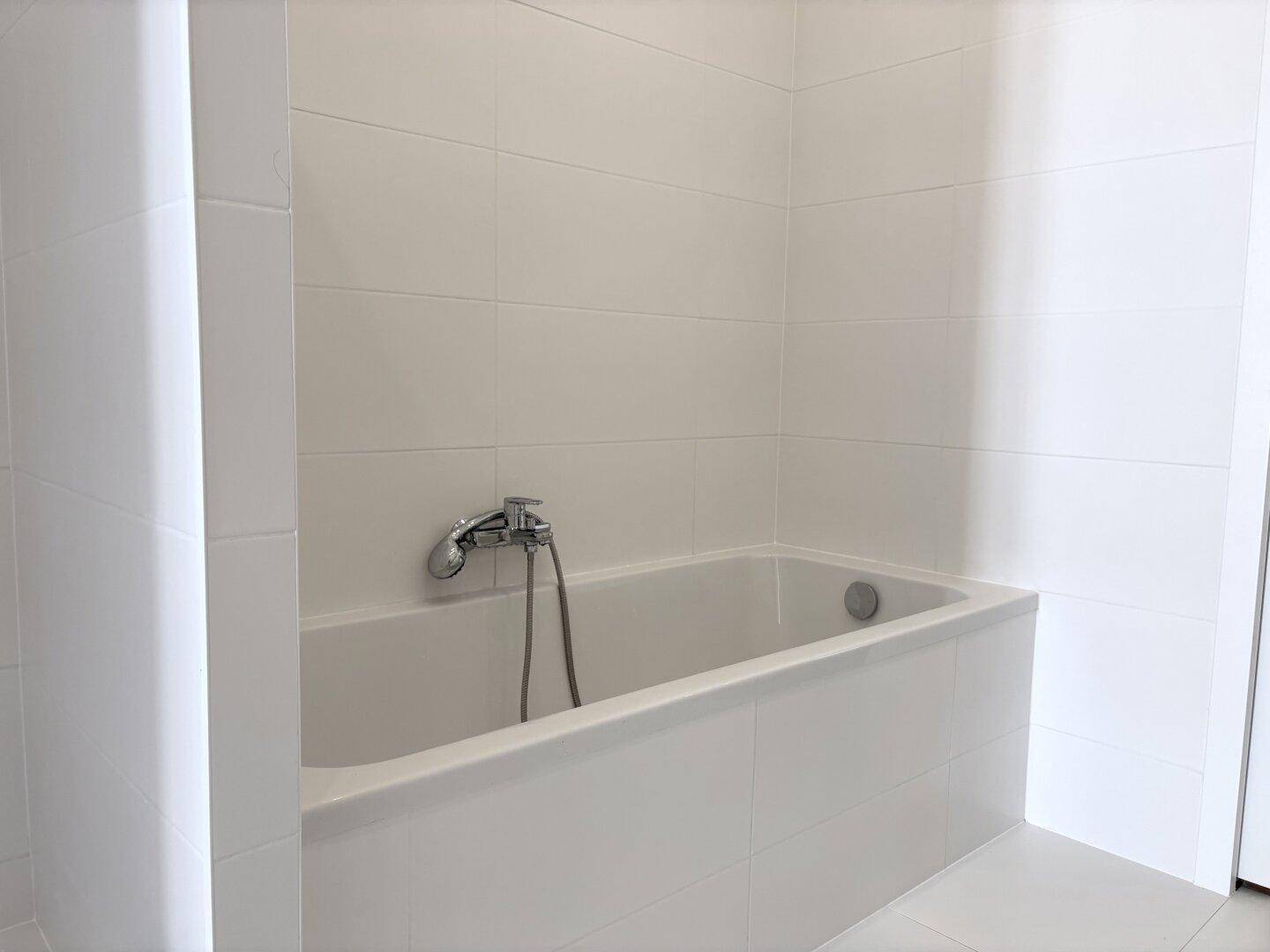 Eingebaute Badewanne mit Duscharmatur in einem modern gefliesten Badezimmer.