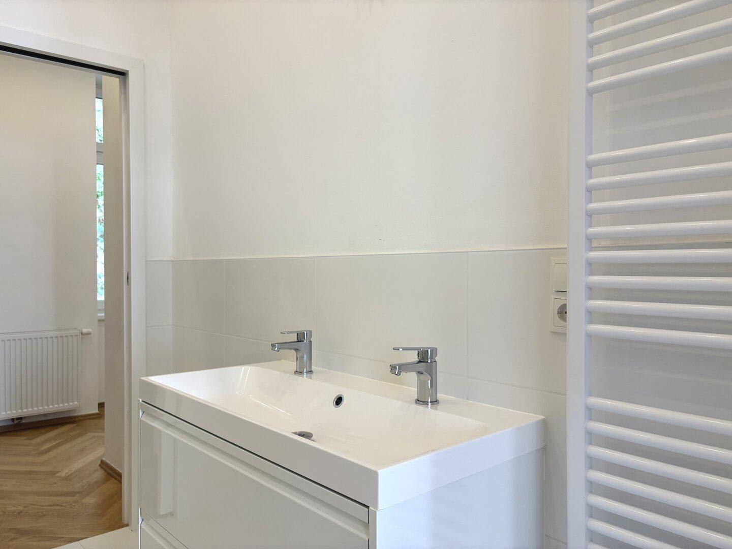 Modernes Doppelwaschbecken mit zwei Armaturen und einem beheizten Handtuchhalter im Badezimmer.
