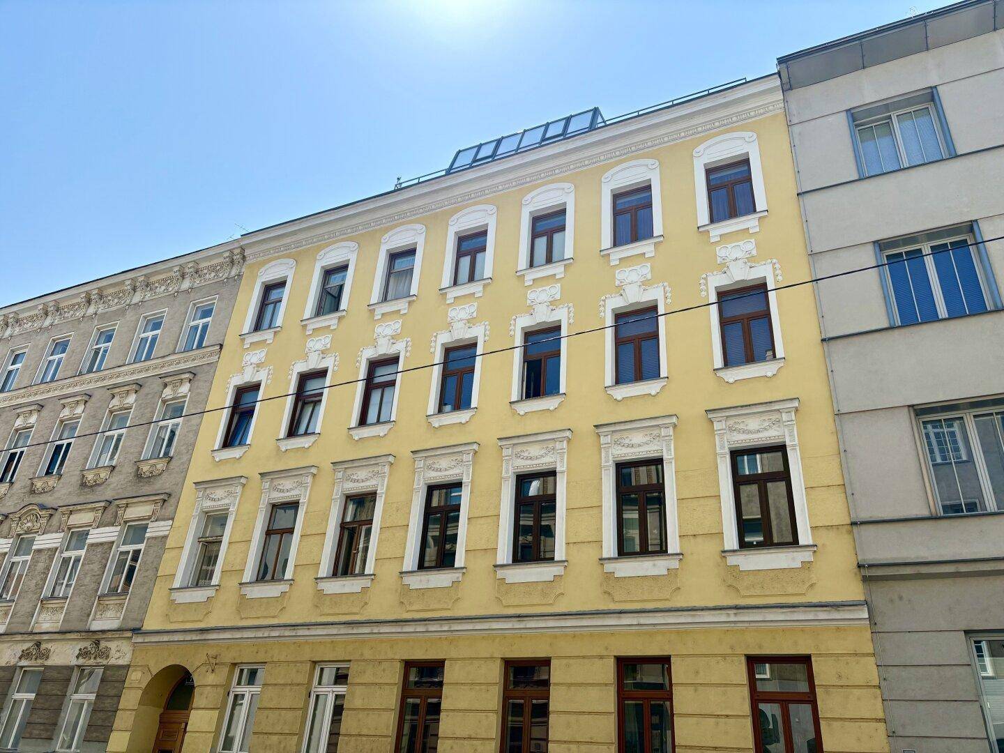Historische Fassade eines Mehrfamilienhauses in Gelb mit vielen Fenstern und Stuckverzierungen.