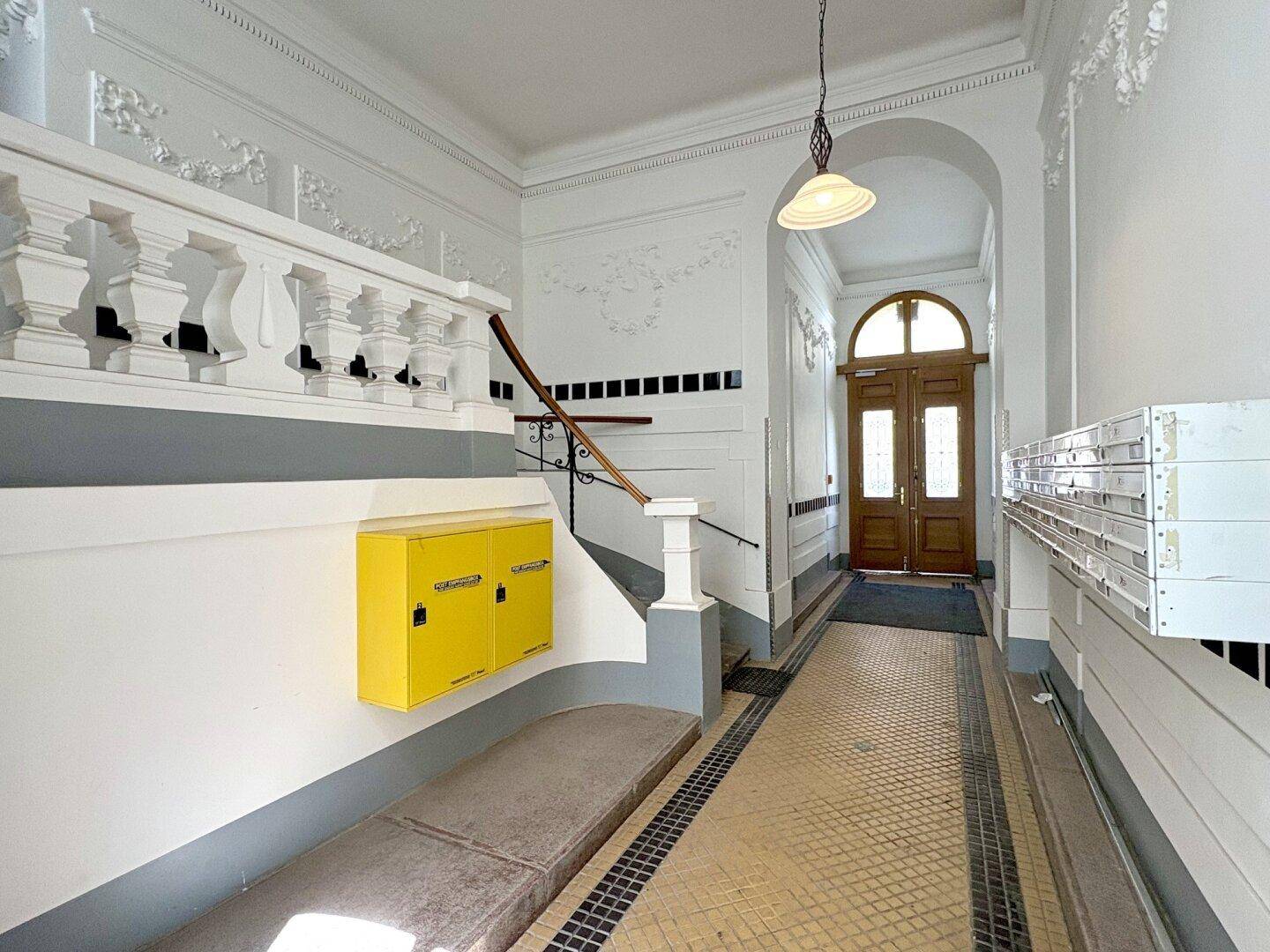 Historischer Eingangsbereich mit Treppe, verzierten Geländern und gemustertem Fliesenboden.