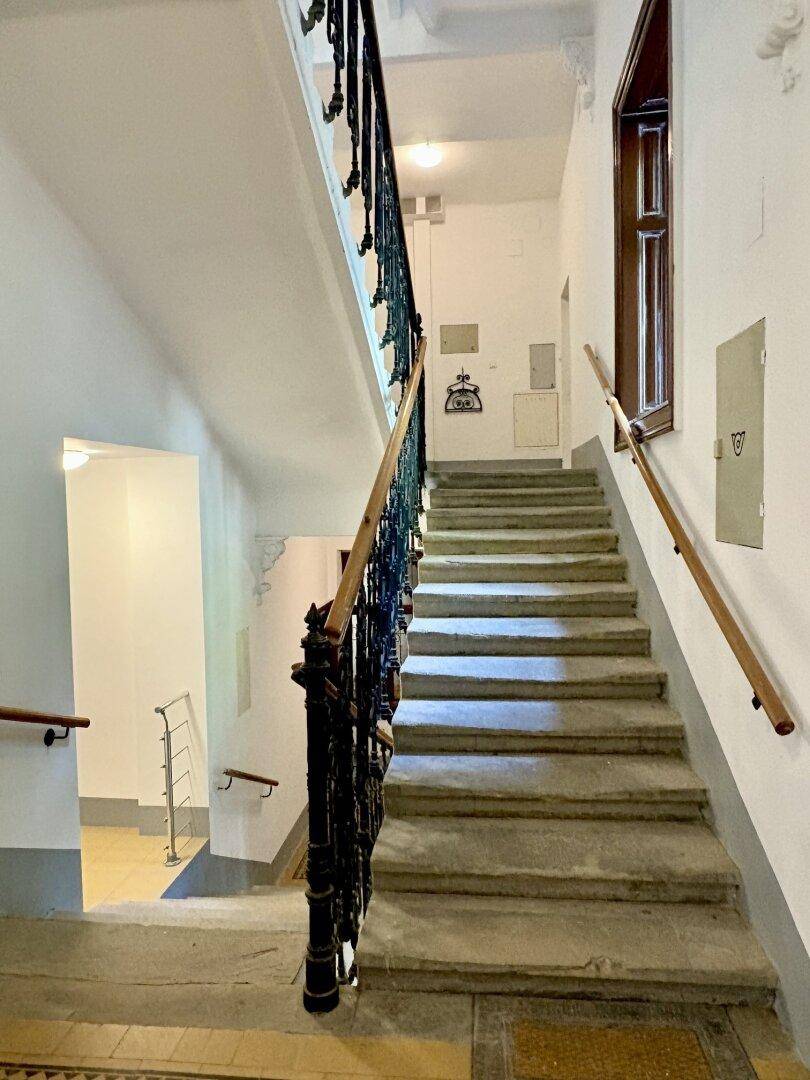 Historisches Treppenhaus mit schmiedeeisernem Geländer und Steinstufen in einem Altbau.