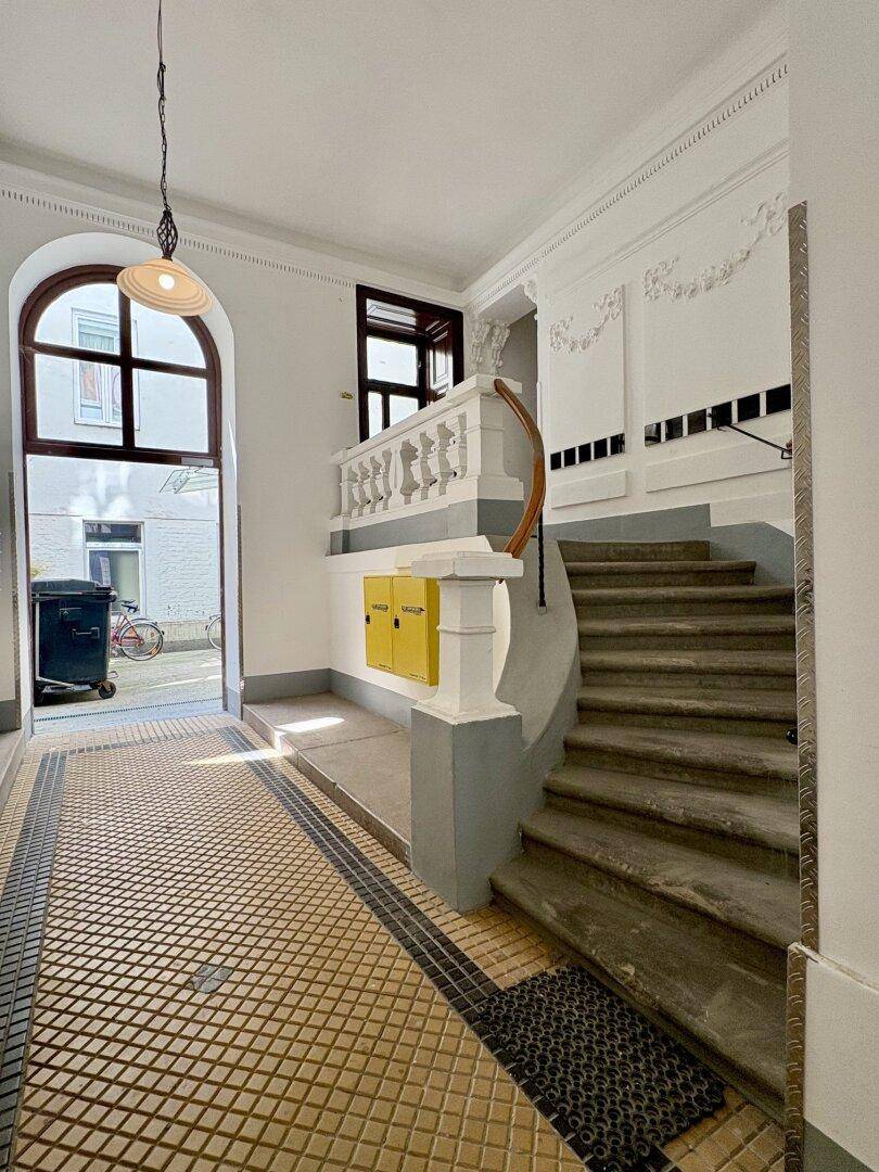 Historischer Eingangsbereich mit Treppe, verzierten Geländern und gemustertem Fliesenboden.