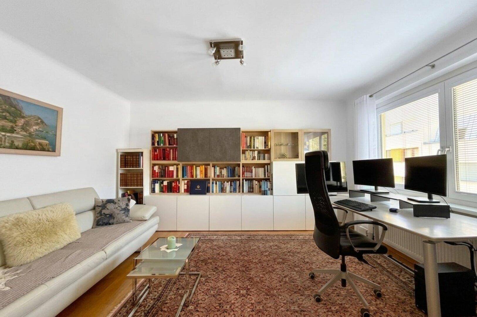 Geräumiges Arbeitszimmer mit großem Bücherregal, Schreibtisch und bequemer Couch.