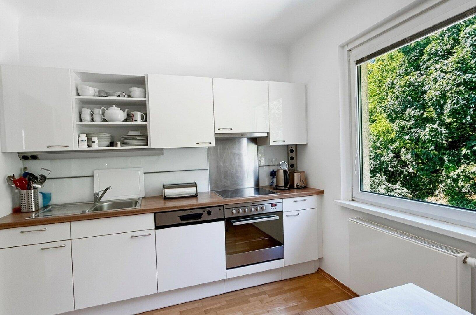 Funktionale Küche mit weißen Schränken, Holz-Arbeitsplatte und Fenster mit Blick ins Grüne.