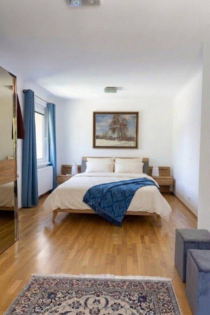 Helles Schlafzimmer mit Holzboden, Doppelbett und einem großen Spiegel.